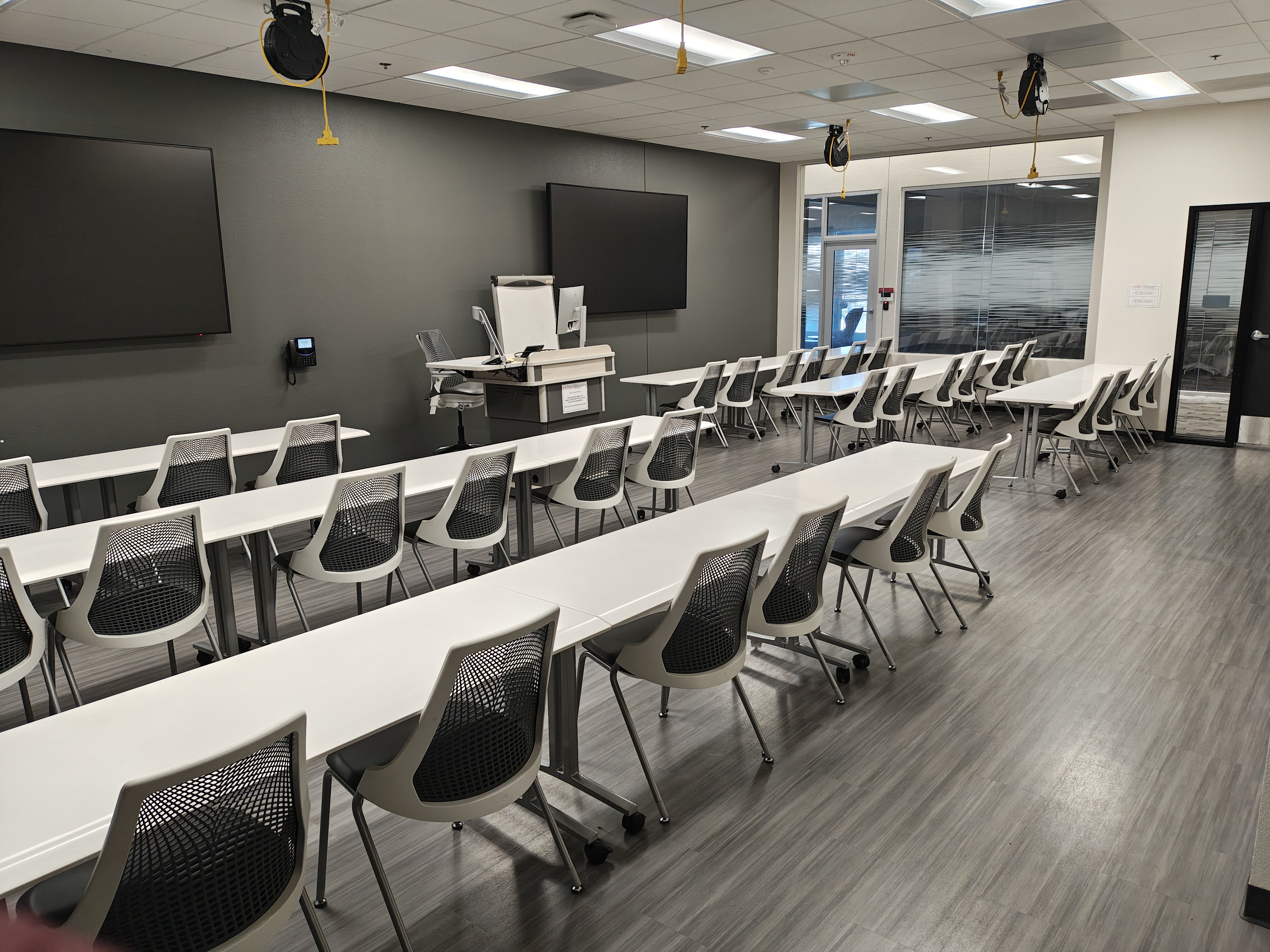 Empty rows of chairs and tables with two TV screens 