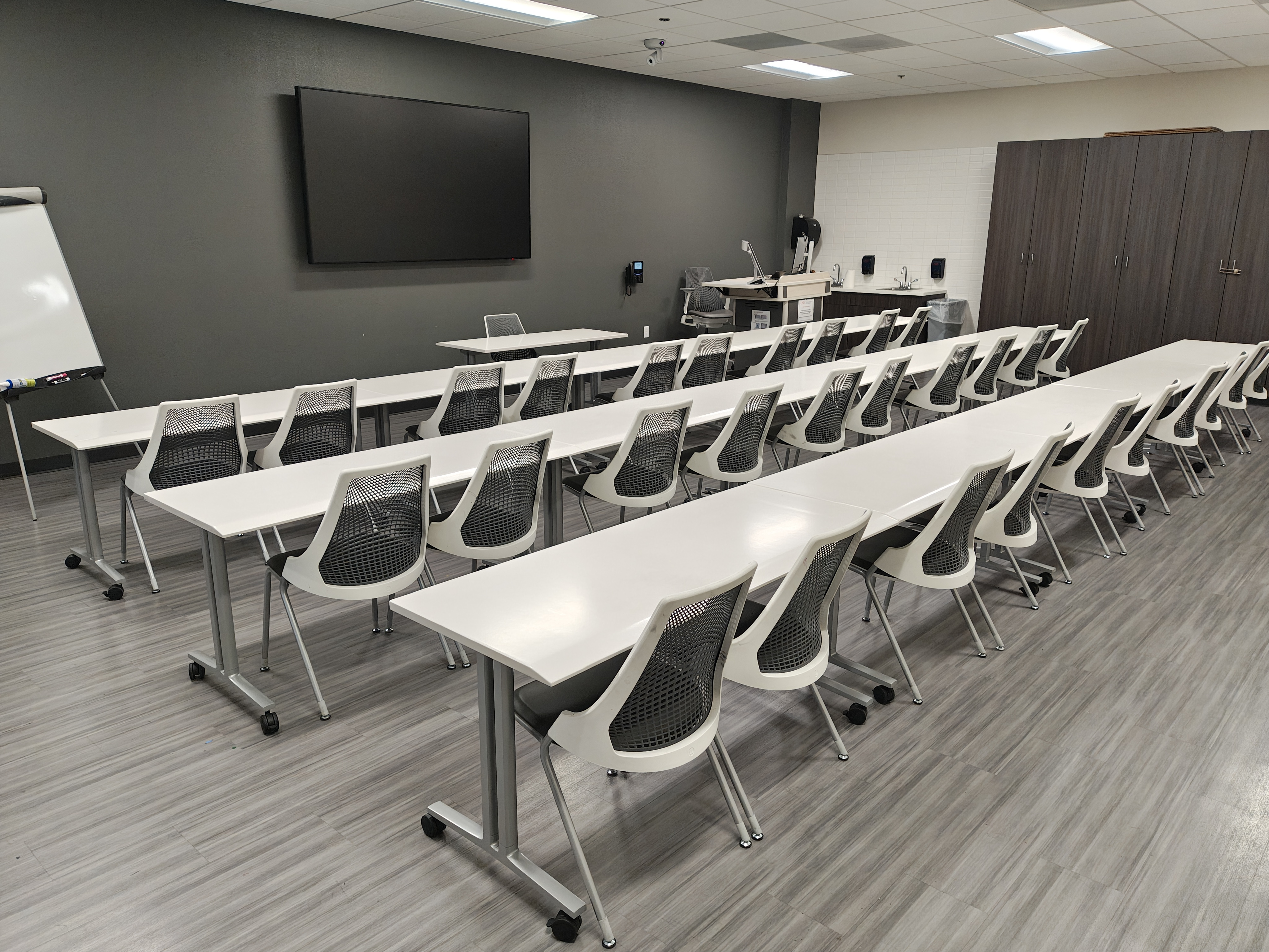Empty classroom with rows of chairs and tables, a TV screen, and a lectern 